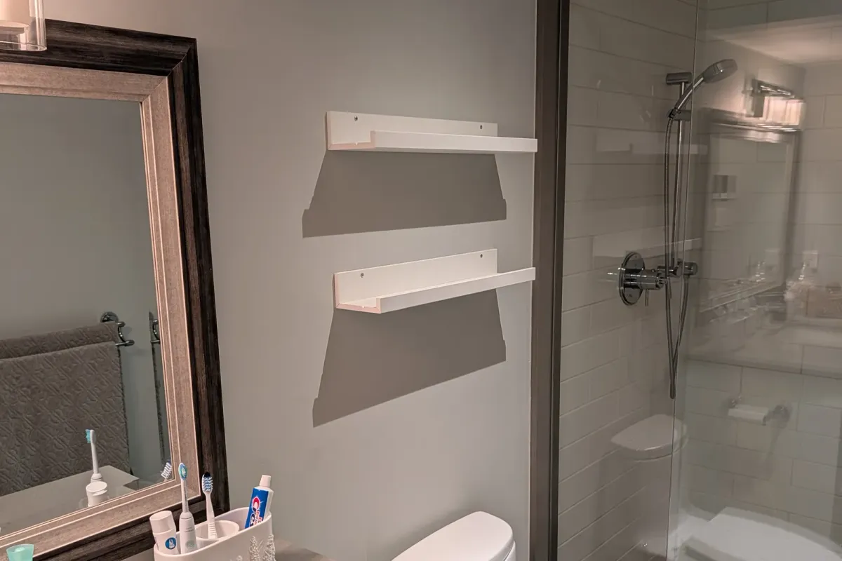 Two white floating shelves mounted on the same wall, beside the mirror and the shower