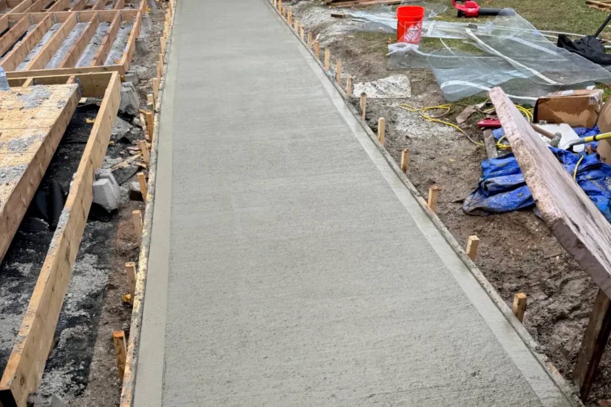 Freshly poured concrete walkway between its wooden forms, beside deck framing