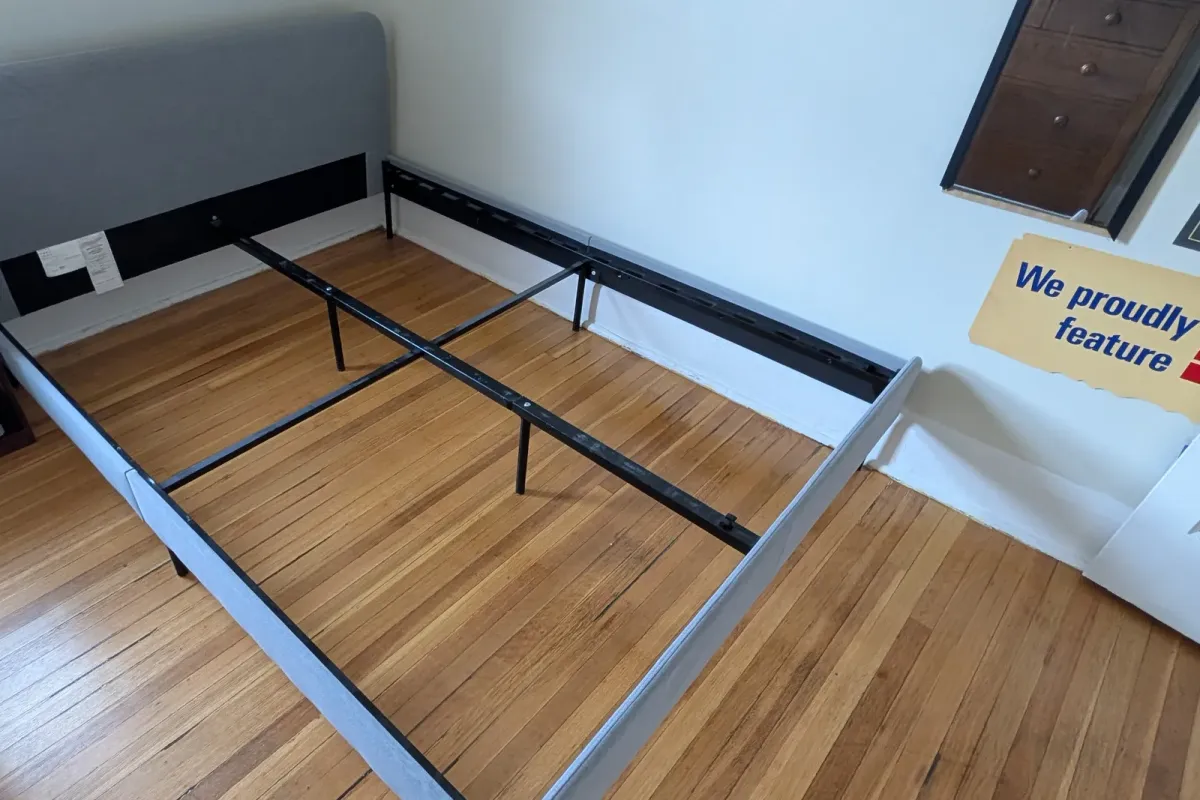 Upholstered bed frame partly taken apart in a bedroom with wood floors
