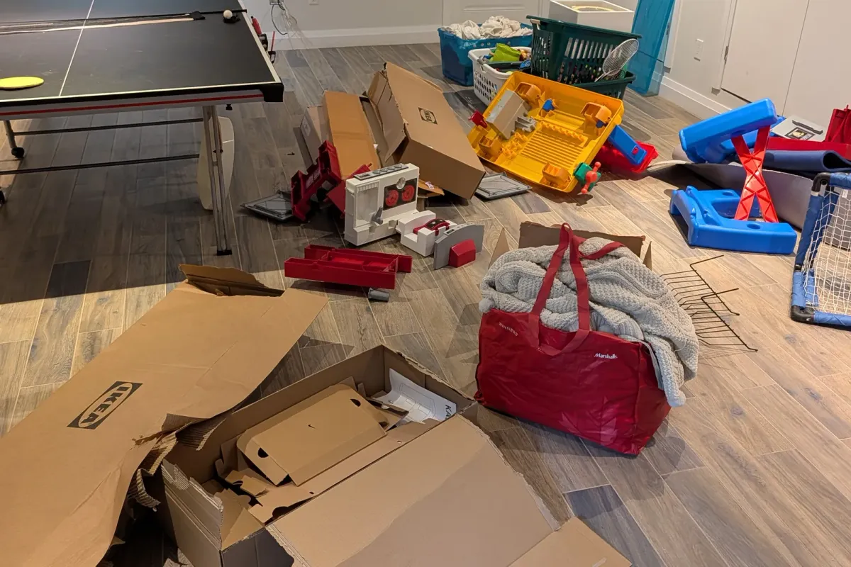 Basement rec room floor covered in toys, boxes and packaging beside a ping-pong table