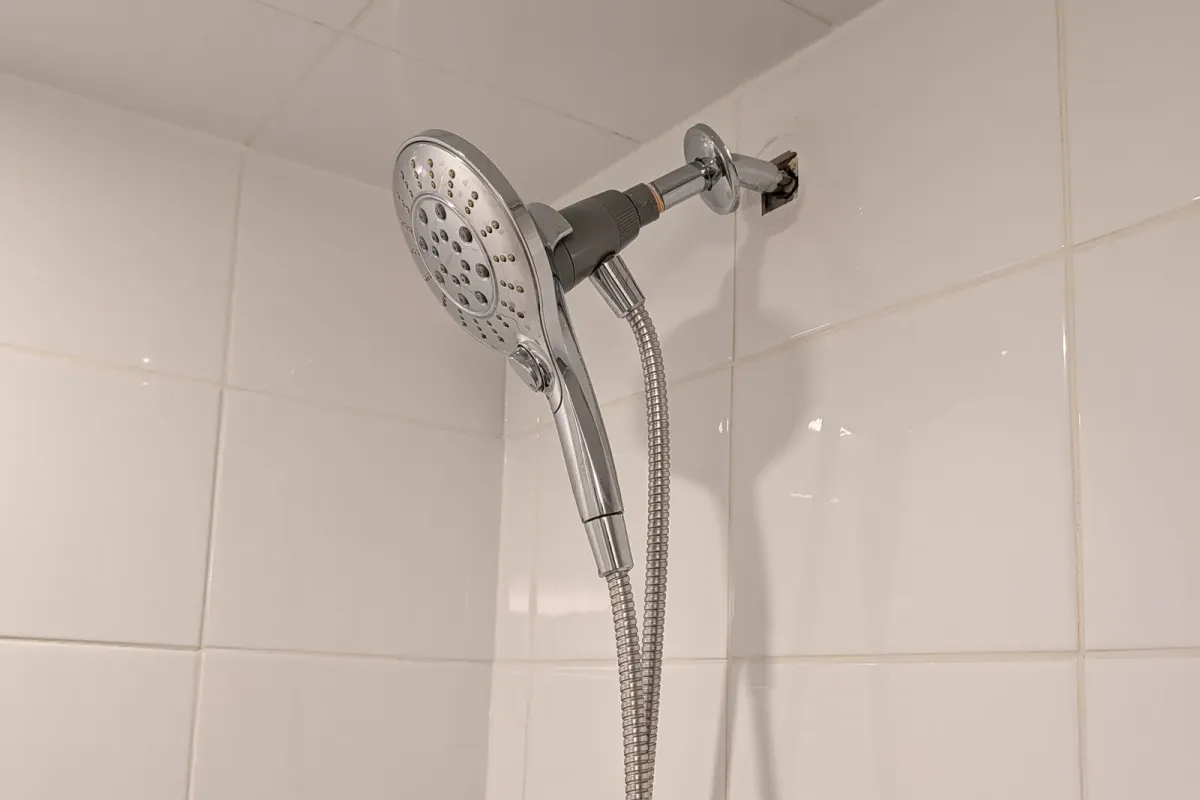 Hand shower and its holder on a shower arm against white tile